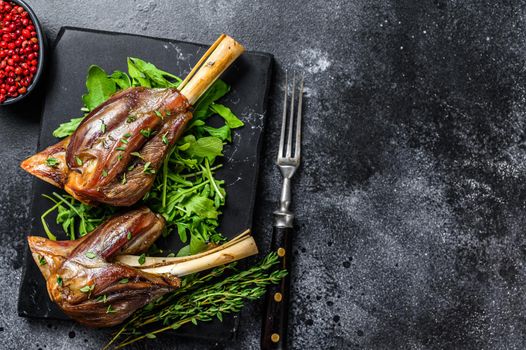 Stew goat Shanks on a marble board with arugula. Black background. Top view. Copy space.