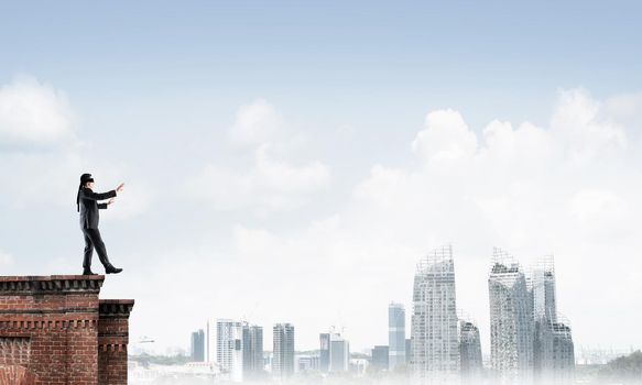 Businessman with blindfolder on eyes walking on building top