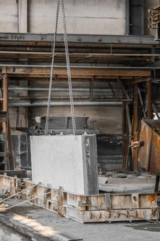 A large concrete plate on a lifting mechanism with a chain in the reinforcement production of an industrial enterprise.