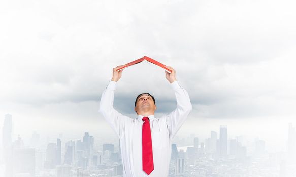 Senior businessman holding open diary overhead as roof. Man in white shirt and tie standing on cloudy cityscape background. Education and professional knowledges. Time management and day planning.