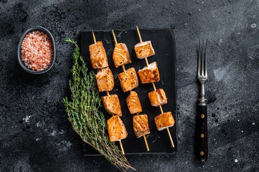 Roasted salmon kebab skewers on marble board. Black background. Top View.