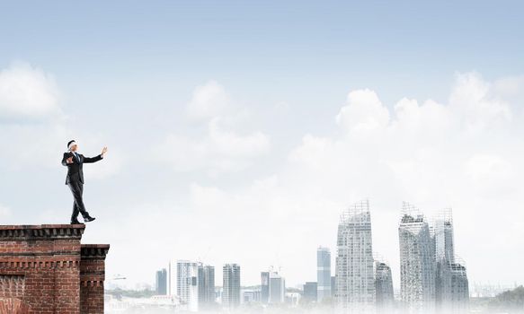Businessman with blindfolder on eyes walking on building top