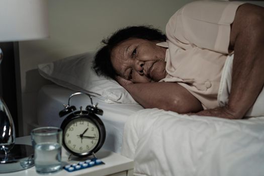 Old woman suffering from insomnia is trying to sleep in bed at night