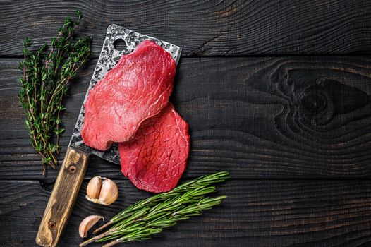 Raw marble beef meat fillet steak on butcher cleaver. Black wooden background. Top view. Copy space.