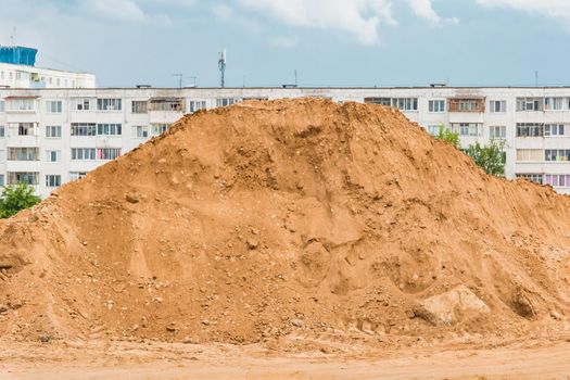 Large pile of sand nature material at a construction site against the background of old multi-storey buildings.