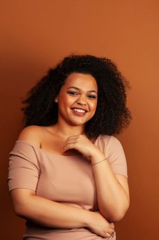 pretty young african american woman with curly hair posing cheerful gesturing on brown background, lifestyle people concept close up