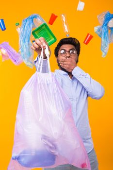 Environmental pollution, plastic recycling problem and waste disposal concept - scared man covering his mouth with hand. He is holding garbage bag on yellow background