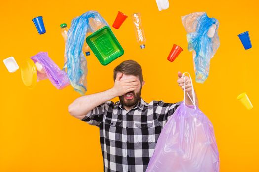 Environmental pollution, plastic recycling problem and ecology problem concept - sad man holding garbage bag and covering his eyes with palm on yellow background