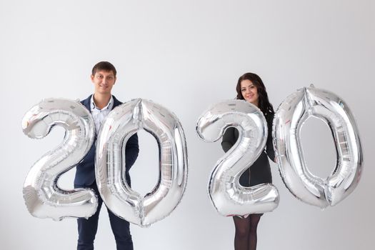 New year, celebration and holidays concept - love couple with sign 2020 made of silver balloons for new year on white background.