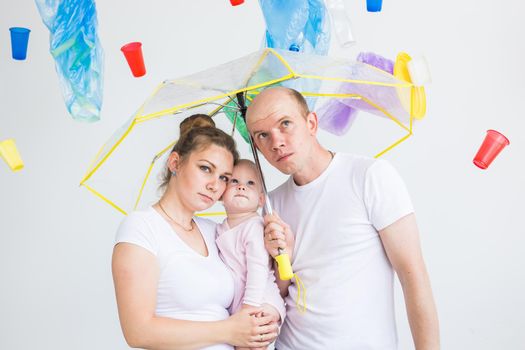 World Environment Day, plastic recycling problem and environmental disaster concept - Sad family hiding from garbage under an umbrella on white background.