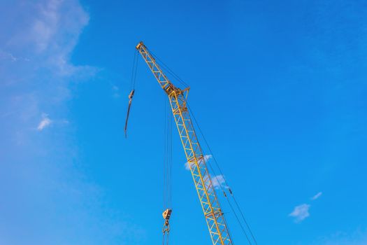 Hoisting machine industrial crane equipment against blue sky at construction site.