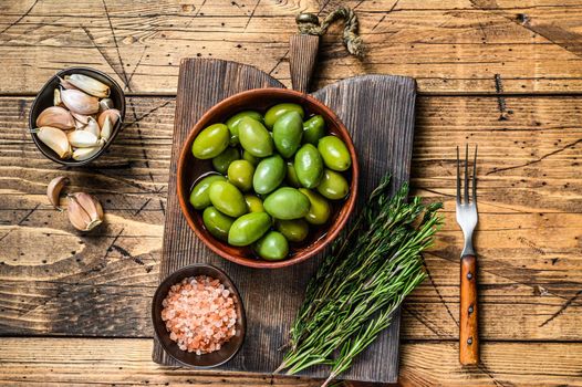 Marinated Green big olives in wooden bowl with oil. wooden background. Top view.