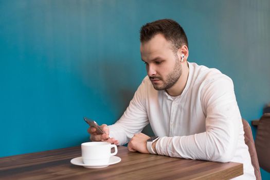 Young businessman in a white shirt looks at the phone and drinks coffee.