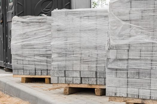 A pile of new paving slabs on a wooden pallet wrapped in plastic wrap. Building materials at the construction site.