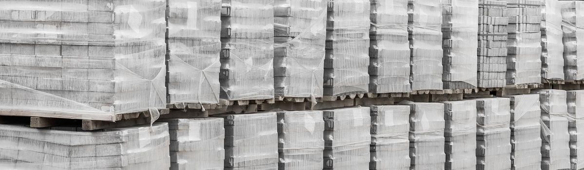 Large pile of packaged paving stone slabs industrial material on pallets at construction site.