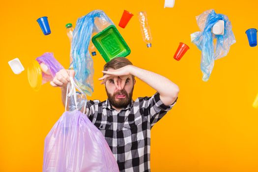 Problem of trash, plastic recycling, pollution and environmental concept - man carrying garbage bag on yellow background. Bad smell of garbage.