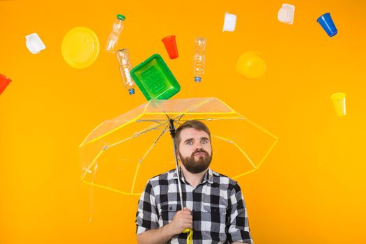 Problem of trash, plastic recycling, pollution and environmental concept - Sad man is standing under trash with umbrella on yellow background.