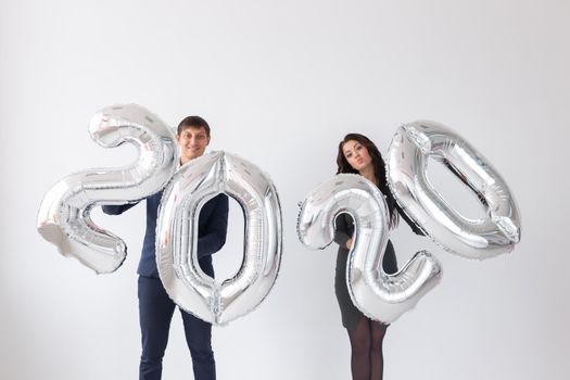 New year, celebration and holidays concept - love couple with sign 2020 made of silver balloons for new year on white background.