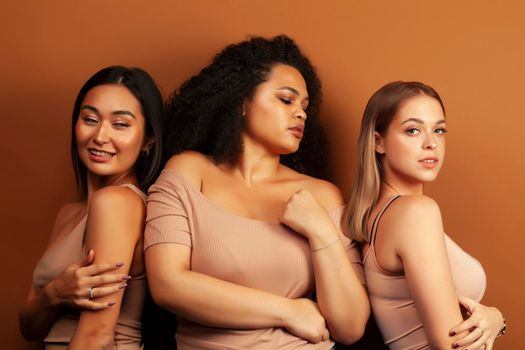 young pretty asian, caucasian, afro woman posing cheerful together on brown background, lifestyle diverse nationality people concept close up