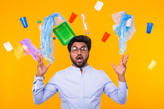 World Environment Day, plastic recycling problem and environmental disaster concept - Terrified Indian man threw up his arms to the sides on yellow background with trash.