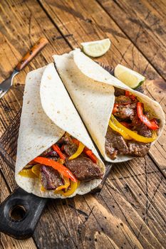 Fajitas Tortilla wrap with beef meat stripes, colored bell pepper and onions and salsa. Wooden background. Top view.