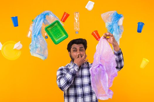 Problem of trash, plastic recycling, pollution and environmental concept - surprised Indian man closing nose because he is felt bad smell from garbage on yellow background