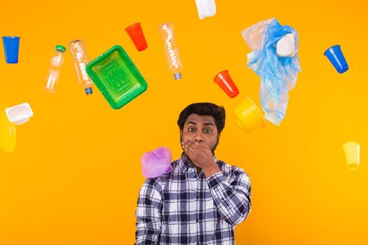 Plastic recycling problem, ecology and environmental disaster concept - scared Indian man covering his mouth with hand on yellow background. Pollution problems.