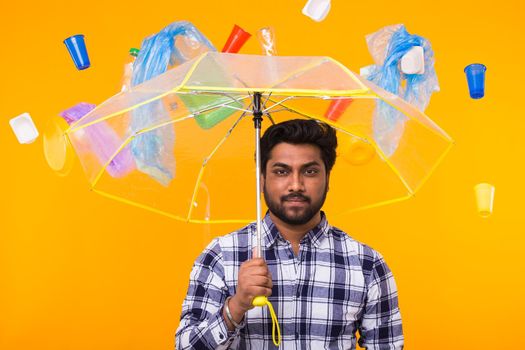 Plastic recycling problem, pollution and environmental disaster concept - Serious Indian man thinking about ecology under an umbrella on yellow background.