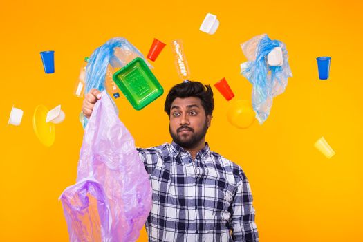 Plastic recycling problem, ecology and environmental disaster concept - Confused Indian man holding garbage bag on yellow background.