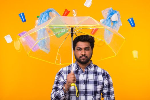 World Environment Day, plastic recycling problem and environmental disaster concept - Sad Indian thinking about ecology and pollution under an umbrella on yellow background.