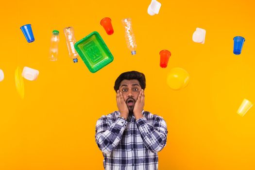 World Environment Day, plastic recycling problem and environmental disaster concept - Terrified Indian man on yellow background with trash.