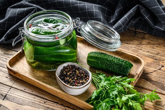 Green salted cucumbers in a glass jar. Wooden background. Top view.