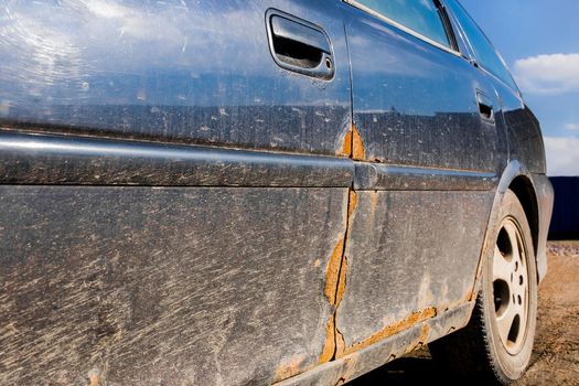 Traces of rust on the driver's metal door of a dirty damaged car, automobile amortization.