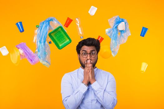 World Environment Day, plastic recycling problem and environmental disaster concept - Scared Indian man standing under trash on yellow background.