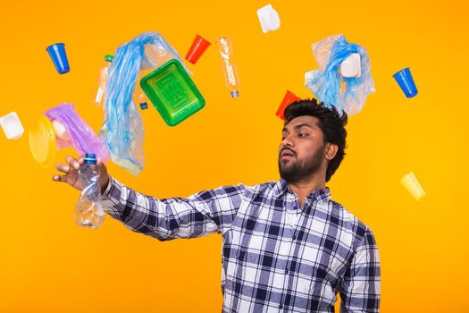 Environmental pollution, plastic recycling problem and waste disposal concept - surprised Indian man holding crumpled plastic bottle on yellow background