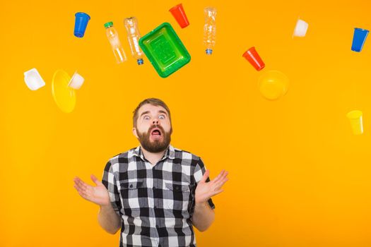 Plastic recycling problem, ecology and environmental disaster concept - Scared man screaming on yellow background with trash. He is worried about ecology disaster.