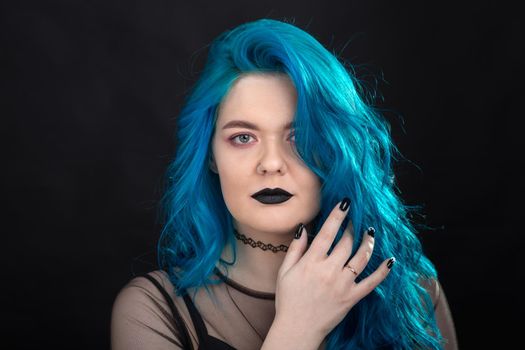 People and fashion concept - Young and attractive woman with black lipstick and blue hair posing over black background.