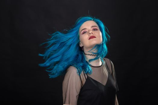 People and fashion concept - Young and attractive woman with black lipstick and blue hair posing over black background.