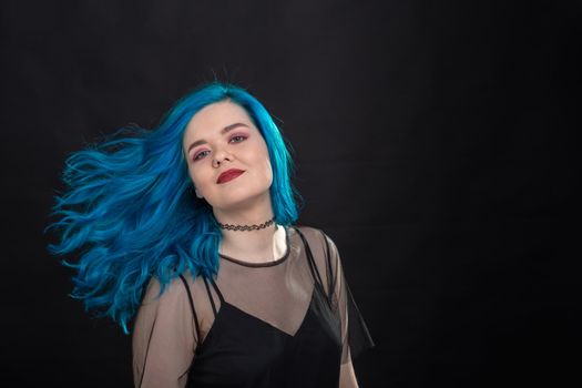people, fashion and hair concept - close-up portrait of young woman in black dress with blue hair on black .