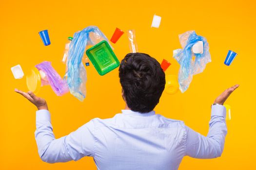 Plastic recycling problem, ecology and environmental disaster concept - Back view of Indian man alarmed from a lot of garbage on yellow background.