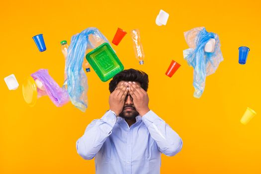 Plastic recycling problem, ecology and environmental disaster concept - Indian man closed his eyes with hands on yellow background. He is terrified by trash problems.