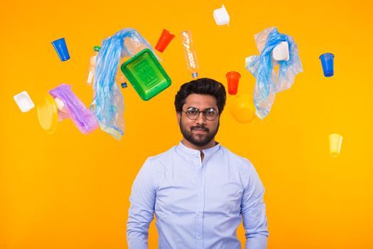 Problem of trash, plastic recycling, pollution and environmental concept - indian man is standing under trash on yellow background.