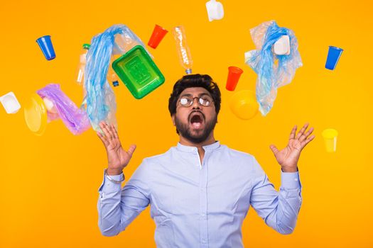 Plastic recycling problem, ecology and environmental disaster concept - Scared Indian man screaming on yellow background with trash. He is worried about ecology disaster.