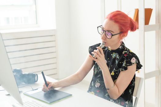 graphic designer concept - Female graphic designer working on computer while using graphic tablet at desk in the office and smoking a vape.