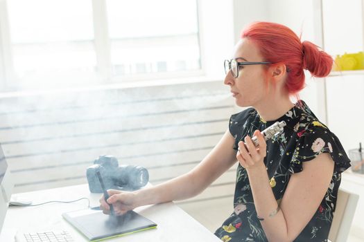 graphic designer concept - Female graphic designer working on computer while using graphic tablet at desk in the office and smoking a vape.