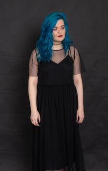 people, fashion and hair concept - full length portrait of young woman in black dress with blue hair on black background.