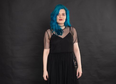 people, fashion and hair concept - full length portrait of young woman in black dress with blue hair on black background.