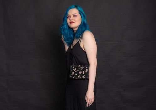 People, fashion and hair concept - full length portrait of young woman in black dress with blue hair on black background.