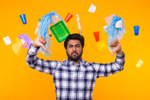 World Environment Day, plastic recycling problem and environmental disaster concept - Sad Indian man making thumbs down on yellow background with trash. Pollution problem.