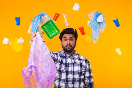 Environmental pollution, plastic recycling problem and waste disposal concept - surprised indian man holding garbage bag on yellow background